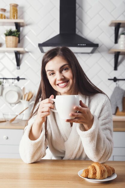 Happy girl having breakfast in the kitchen with croissants and coffee