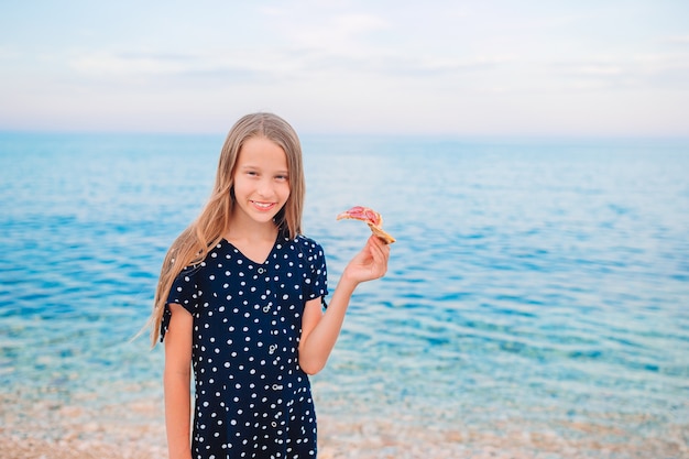 Happy girl having fun on the beach and eating pizza