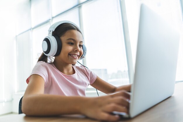 The happy girl in headphone sitting at the table with a laptop