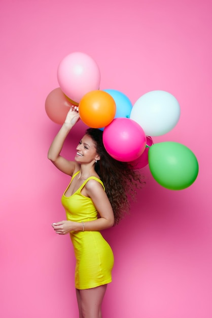Счастливая девушка держит цветные воздушные шарики на желтом фоне