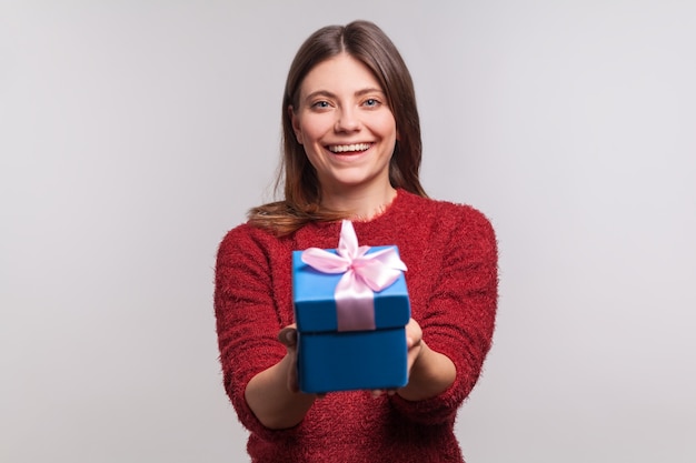 Счастливая девушка держит украшенную упакованную подарочную коробку и смотрит в камеру с зубастой улыбкой