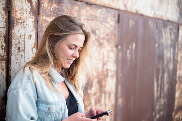 Happy girl holding and using her smartphone alone - caucasian woman playing with her phone - millenial 20s