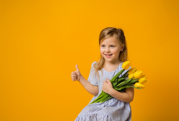 A happy girl holds a bouquet of yellow tulips and shows a class on yellow