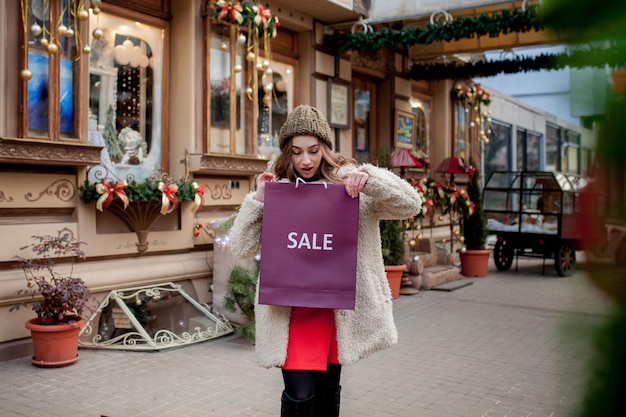 Happy girl holds paperbags with symbol of sale in the stores with sales at Christmas around the city Concept of shopping holidays happiness Christmas Sales