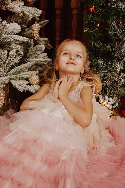 Happy Girl in een roze jurk bij de kerstboom