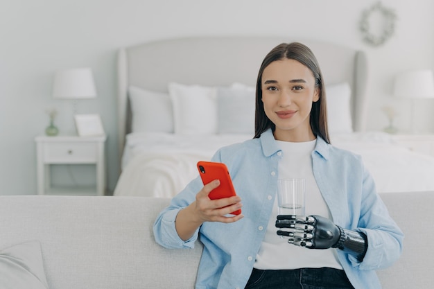 Happy girl is holding glass of water with cyber hand prosthesis Futuristic medical technology