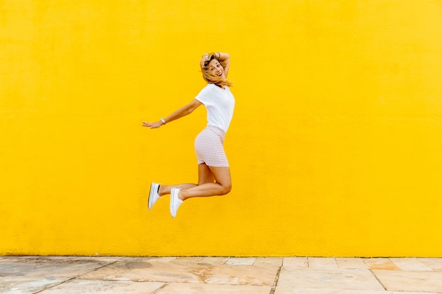 Foto ragazza felice che salta su uno sfondo giallo