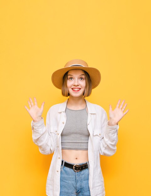 Happy girl in light clothing and sun hat stands on yellow background