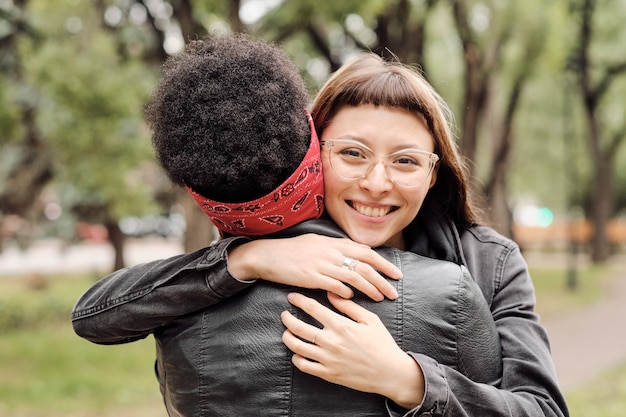Фото Счастливая девушка смотрит на тебя, обнимая свою африканскую подругу на открытом воздухе