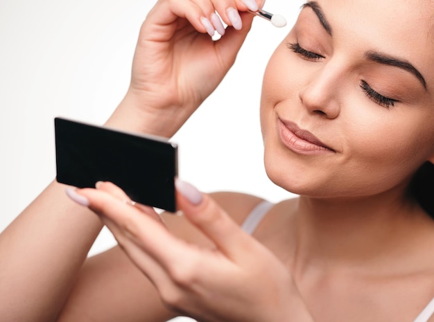 Photo happy girl looking mirror holding brush while applying makeup