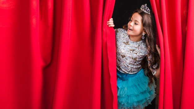 Foto ragazza felice che osserva attraverso la tenda rossa in scena