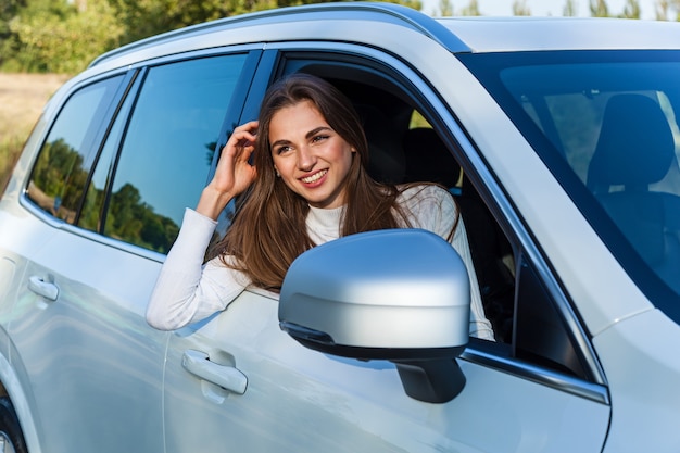 Happy girl looks out the window of a white car and smiles