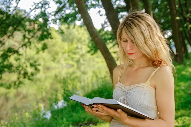 Счастливая девушка на природе читает книгу в парке