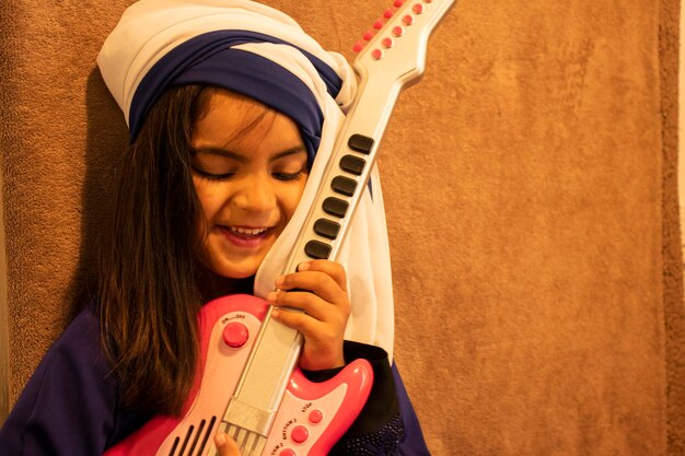 Happy girl playing guitar against wall