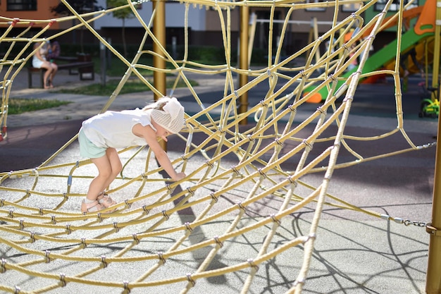 A happy girl playing in a rope net on the playground Modern playground Active recreation in the city