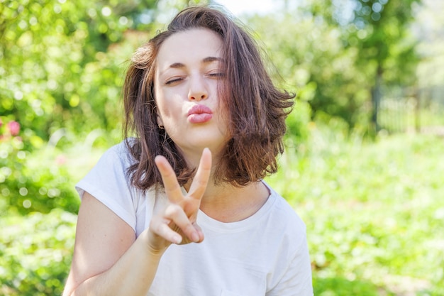 Happy girl posing with kiss face expression. Beauty portrait young happy positive brunette woman on park