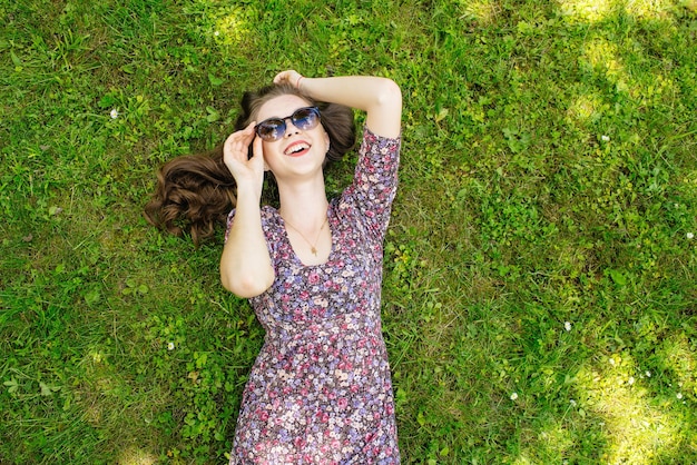 Счастливая девушка отдыхает на лужайке, лежа на спине и глядя в небо