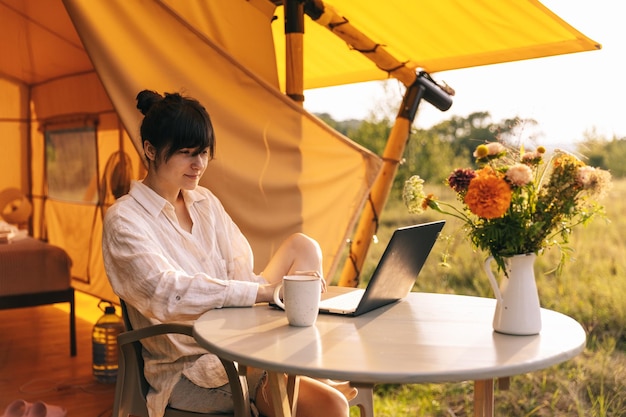 Photo happy girl relaxing on vacation camping young woman sitting in camp tent young female caucasian model reading text and work on notebook