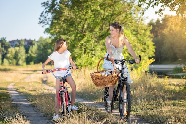 Photo happy girl riding on bicycle with her mother in meadow at sunset