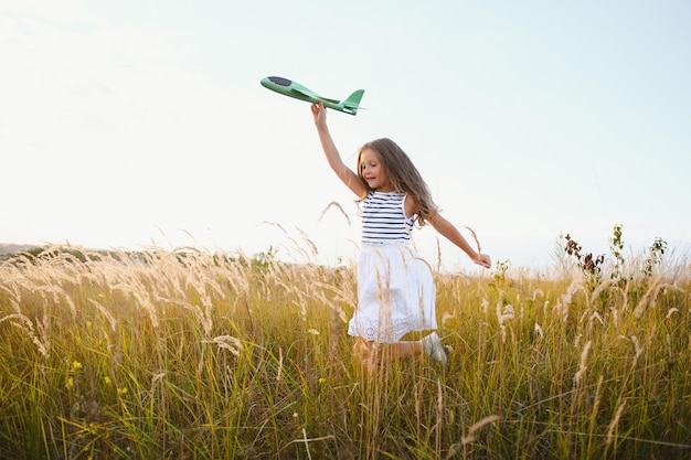 Happy girl runs with a toy airplane on a field in the sunset\
light children play toy airplane teenager dreams of flying and\
becoming a pilot girl wants to become a pilot and astronaut slow\
motion