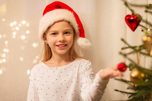 クリスマスツリーを飾っているサンタの帽子をかぶった幸せな女の子