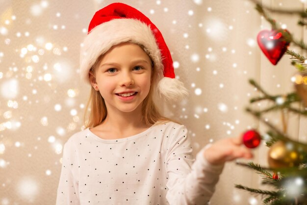 happy girl in santa hat decorating christmas tree