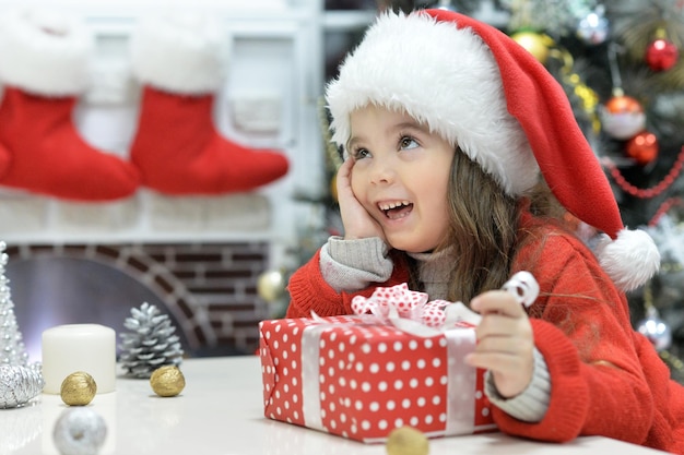 Happy girl in Santa hat sitting with Christmas present