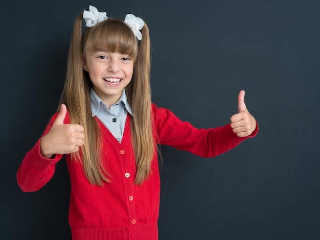 Happy girl showing thumb up gesture in front of a big chalkboard Back to school concept