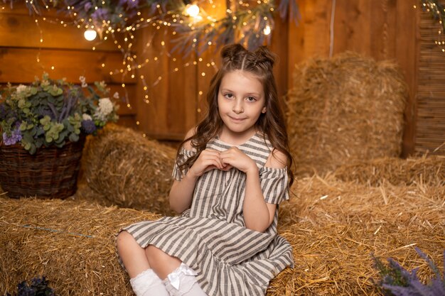 Happy girl sitting in straw sheaves in farm wearing dress