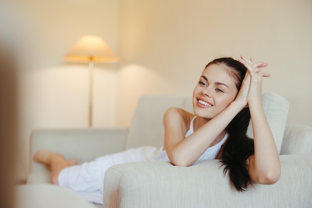 Счастливая девушка улыбается, лежа на диване дома, расслабляясь в домашнем комфорте на солнце