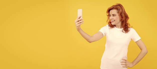 幸せな女の子の笑顔にモバイル カメラ携帯電話の黄色の背景ビデオ selfie モックアップ コピー スペースを持つ女性分離顔ポートレート バナー