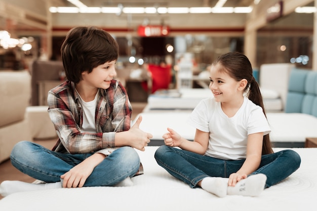 Happy Girl and Smiling Boy Sitting on Bed in Store