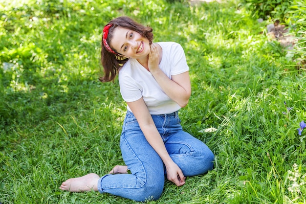 屋外笑顔幸せな女の子。公園や庭の緑の草の壁で休んでいる茶色の髪の美しい若いブルネテ女性。ヨーロッパの女性。肯定的な人間の感情の表情のボディーランゲージ。