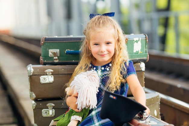 Happy girl at the station in a dress with a toy waiting for the train with an old suitcase