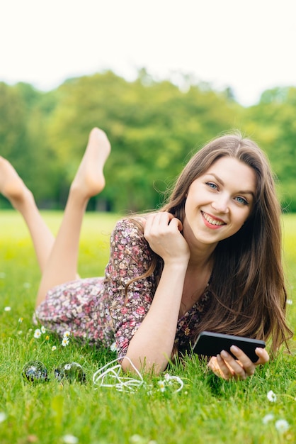 Happy girl or student with smartphone relaxing outdoors in the park