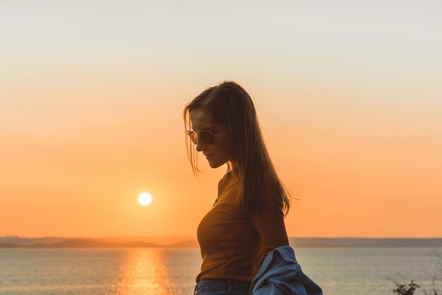 Ragazza felice in abiti eleganti in riva al mare durante il tramonto