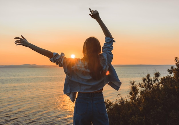 Happy girl in stylish clothes by the sea during sunset