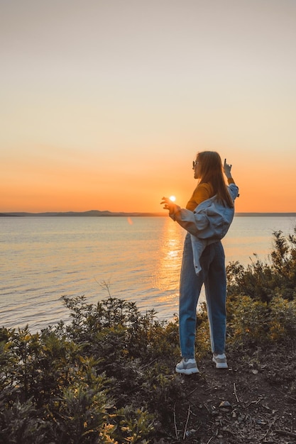 Happy girl in stylish clothes by the sea during sunset