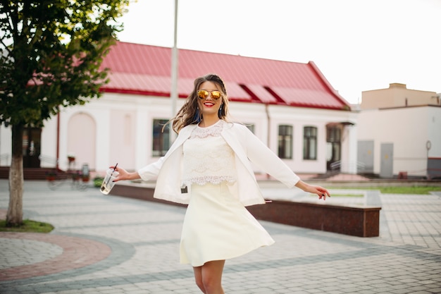 Happy girl in sunglasses in white outlook dancing in the street.