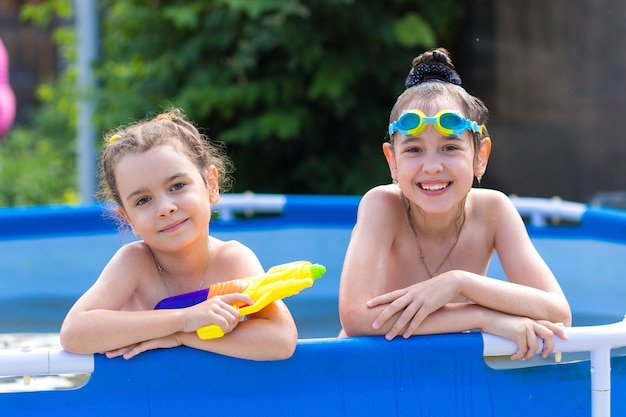 Ragazza felice nella piscina con cornice con occhialini da nuoto e pistola ad acqua.