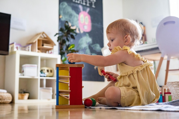 행복한 소녀 유아가 색깔 있는 공에 나무 망치를 치는 초기 개발 생태 장난감