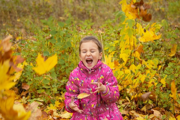 Happy girl tosses leaves in the park in autumn