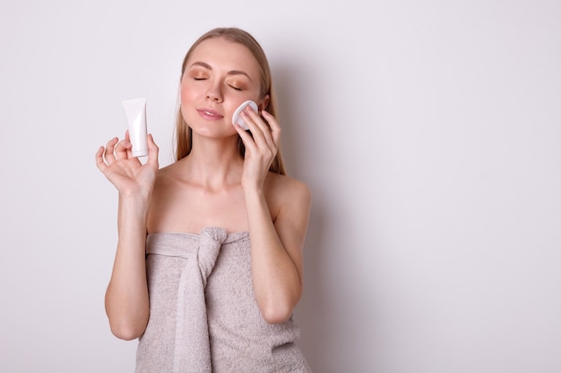 Happy girl in towel cleans face with cotton pad