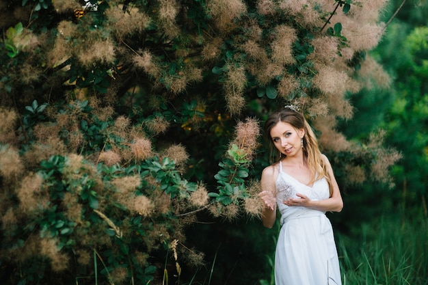 Happy girl in a turquoise long dress in a green park on a background of herbs, trees and rose bushes