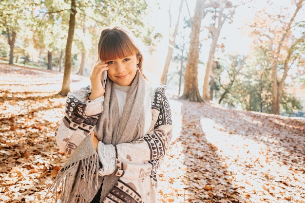 사진 공원에서 가을 동안 스마트 폰을 사용하는 행복한 소녀, 가을에 휴대전화로 통화하는 여자. 야외에서 영상통화를 하고 좋은 소식을 듣습니다.