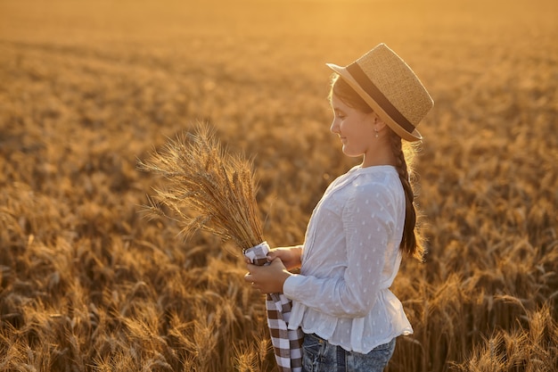 Happy girl walking in golden wheat, enjoying the life in the field. Nature beauty, field of wheat. Cute little girl with golden ears in the hands. Selective focus