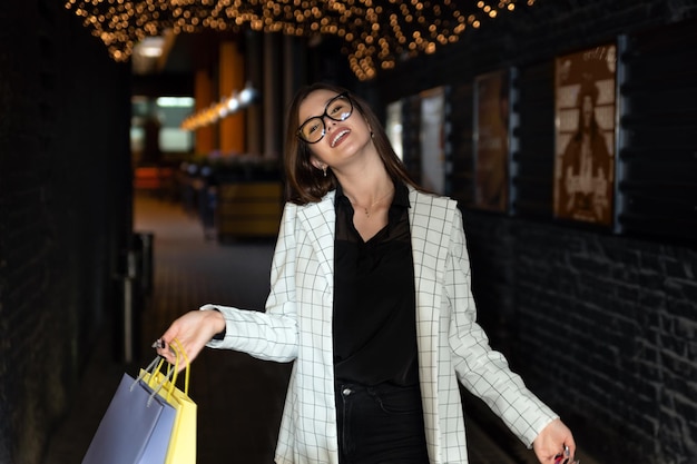 Happy girl walks in evening city with paper bags in her hands Successful shopping