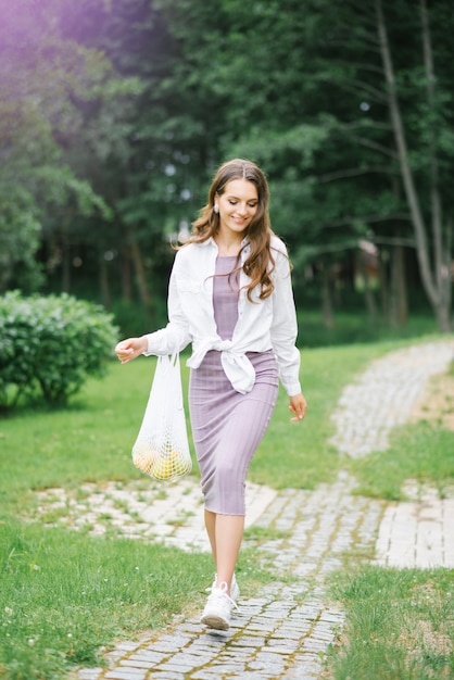 Una ragazza felice cammina nel parco con un sacchetto di frutta riutilizzabile ecologico