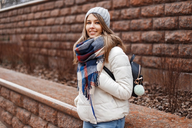 Happy girl in a white jacket with a scarf travels around the city