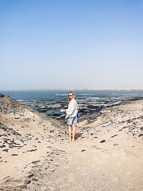 澄んだ青い空と海の水の背景に対して夏の日のビーチで休暇を楽しんで後ろから見た白いシャツの幸せな女の子コピースペース旅行コンセプト自然の風景